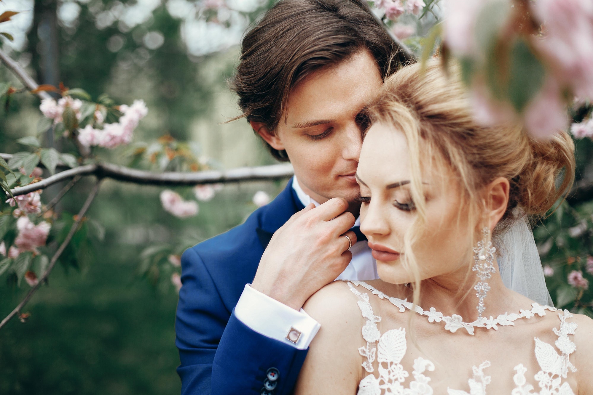 bride-and-groom-embracing-and-kissing-in-park-among-magnolia-flowers.jpg