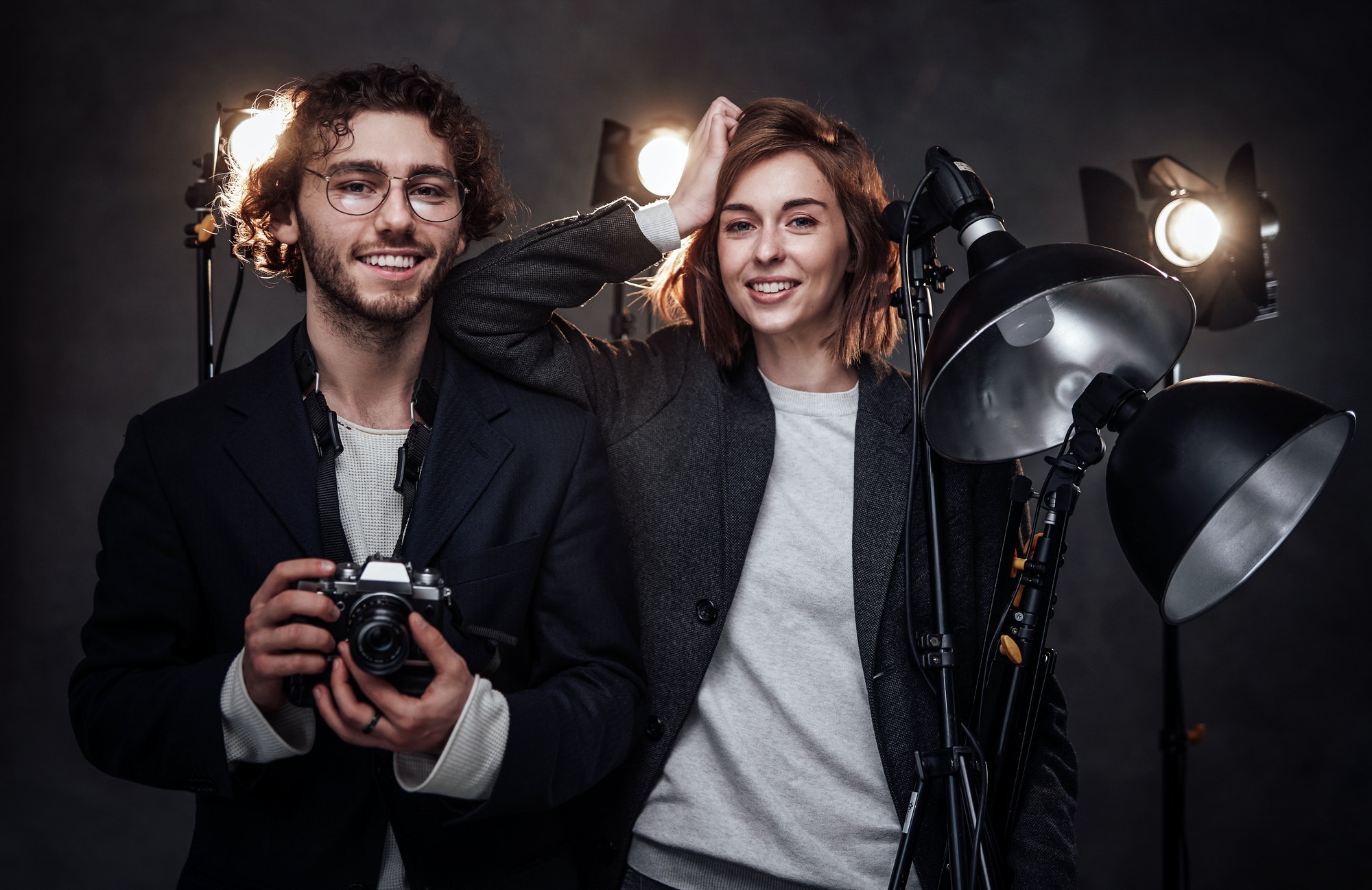 the-team-of-two-photographers-holds-a-digital-camera-and-lighting-equipment-posing-in-studio.jpg